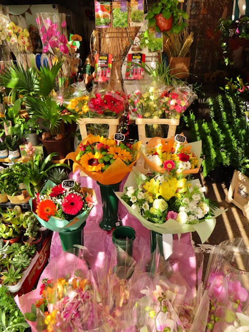 A vibrant display of freshly arranged floral bouquets featuring bright and cheerful flowers such as gerbera daisies, chrysanthemums, and roses in shades of yellow, orange, pink, and red. The bouquets 